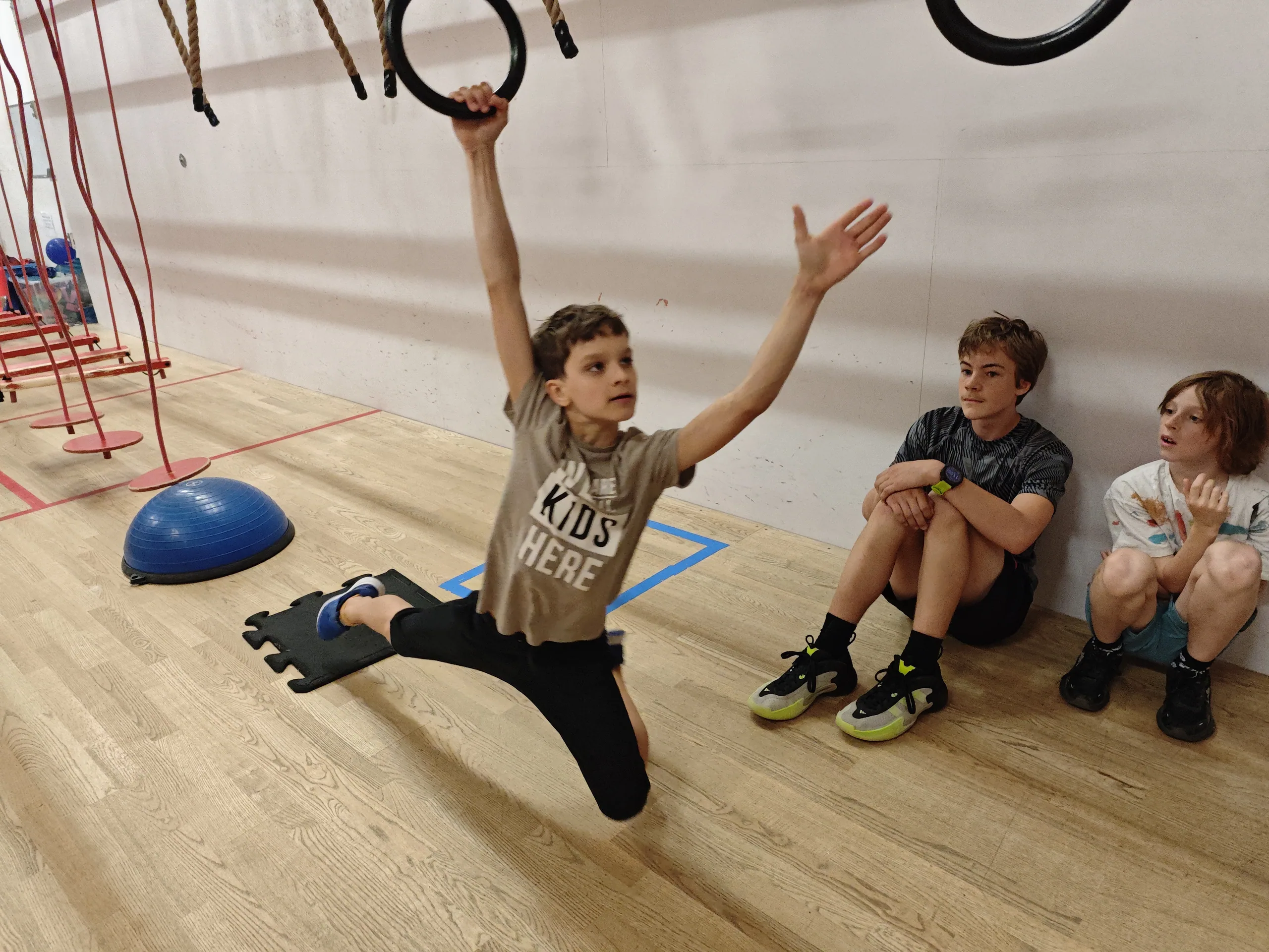 Chłopiec zwisający na kółkach gimnastycznych na sali Ninja Club